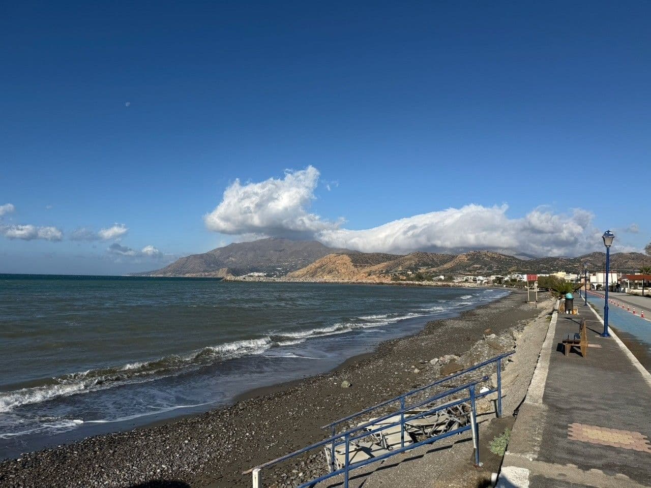 Small waves on the beach by the promenade, clouds building over the mountains